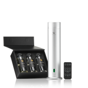 Diffuseur aromatique argenté avec télécommande, posé à côté d'un coffret noir contenant trois flacons de fragrances hôtelières.